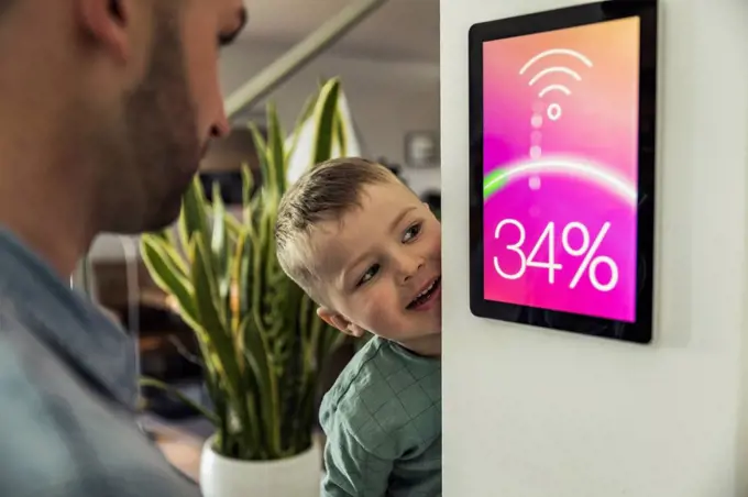 Smiling boy with father looking at smart thermostat in home