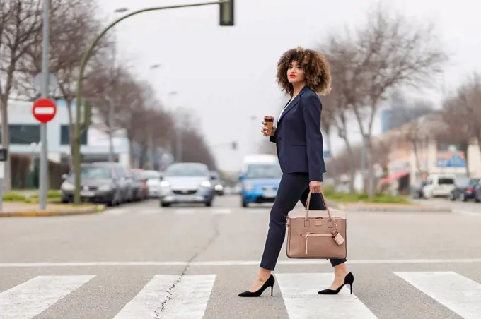 Well-dressed businesswoman with purse crossing road in city