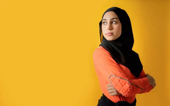 Arab woman with looking away with arms crossed against yellow background