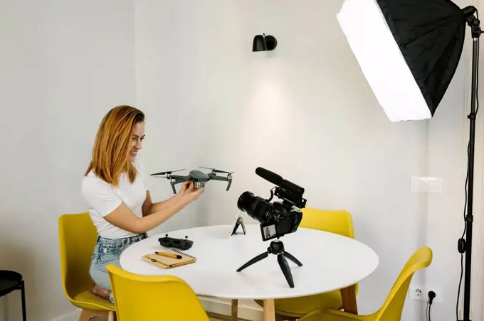 Smiling female influencer with drone vlogging by wall at home