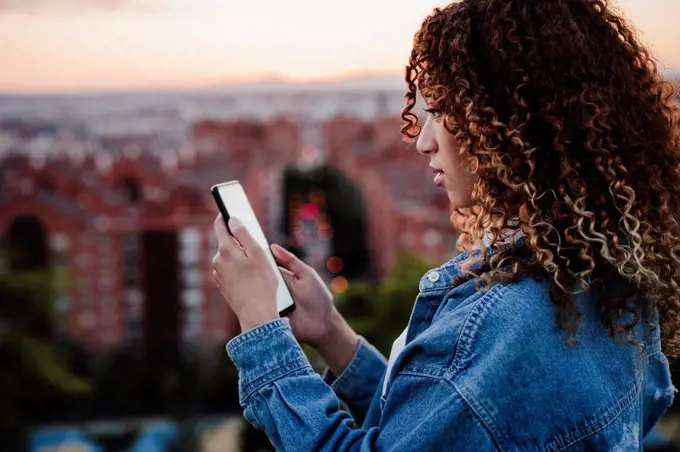 Hispanic woman using smart phone during sunset