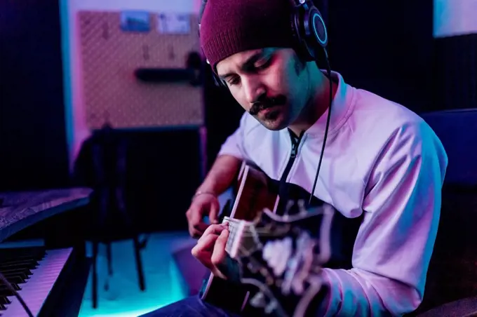Male guitarist wearing knit hat playing guitar at home studio