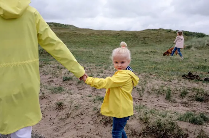 Cute daughter holding hand of mother while walking on hill