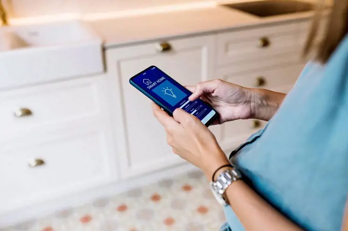 Pregnant woman using mobile phone with smart home app at kitchen