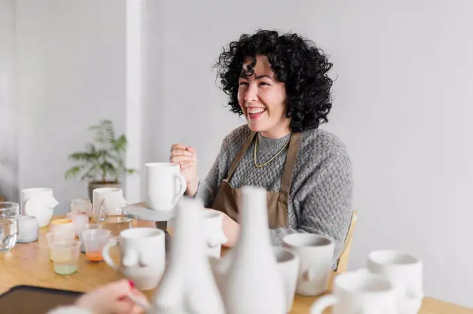 Cheerful female artist with ceramic products at workplace
