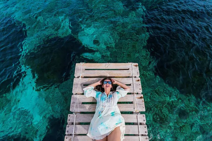 Happy woman wearing sunglasses lying on jetty amidst water