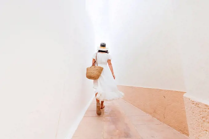 Mature woman wearing hat walking on footpath amidst walls