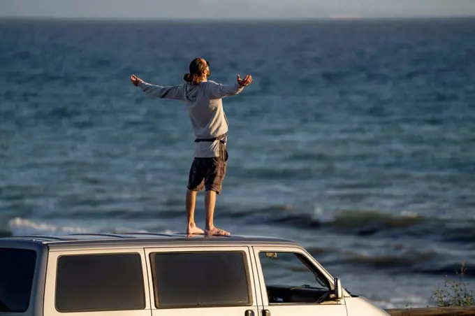 Carefree man standing with arms outstretched on mini van roof