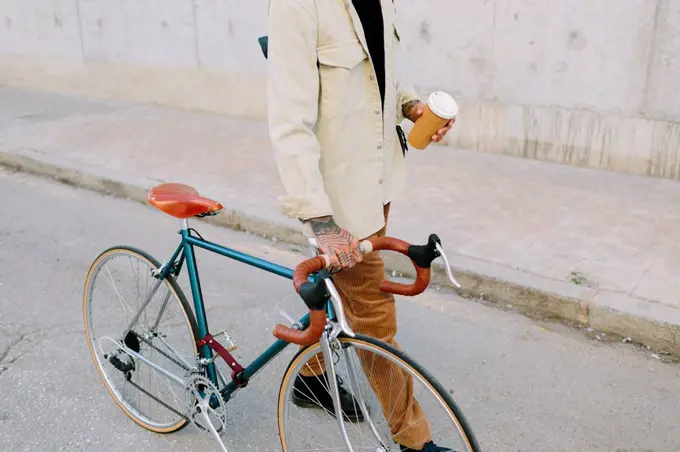 Man holding reusable coffee cup while wheeling bicycle on road
