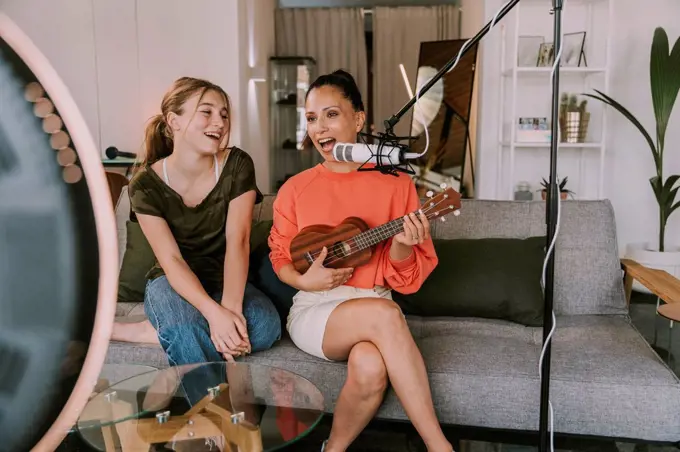 Girl sitting on sofa with female friend playing ukulele at home