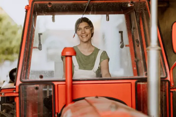 Smiling female farm worker sitting in tractor seen through windshield
