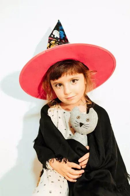 Girl with stuffed toy wearing Halloween costume by wall