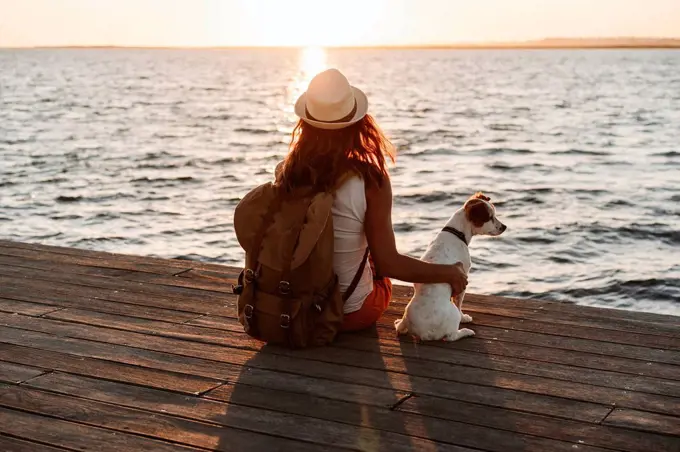 Woman looking at view while sitting by dog on pier