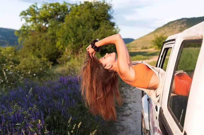 Carefree young woman with long hair leaning out from car window