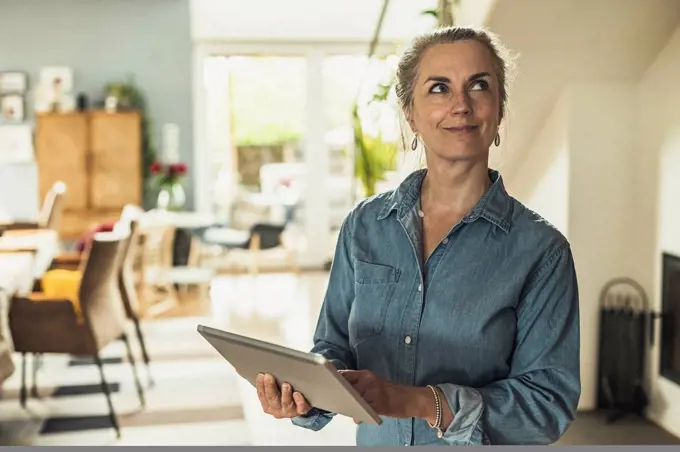 Thoughtful woman with digital tablet standing at home