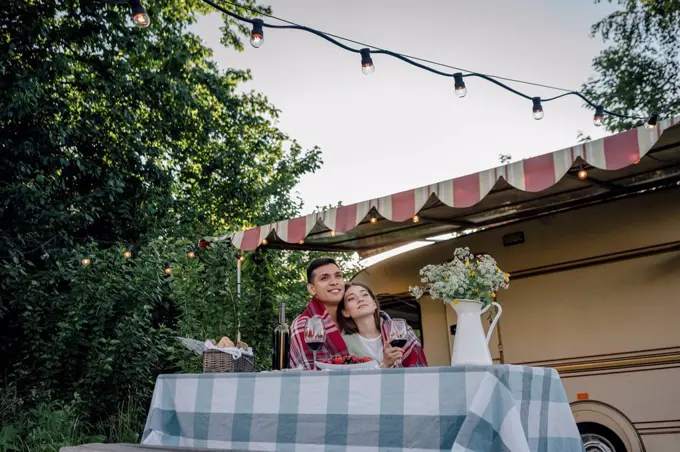 Young couple wrapped in blanket sitting at table by motor home
