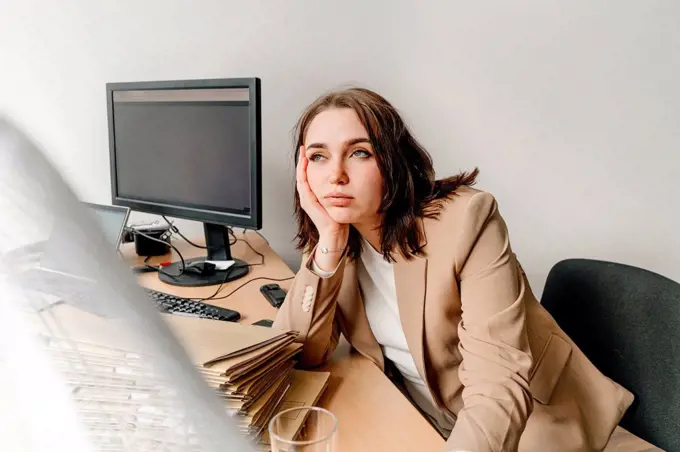 Tired businesswoman with head in hand looking away sitting at desk in office