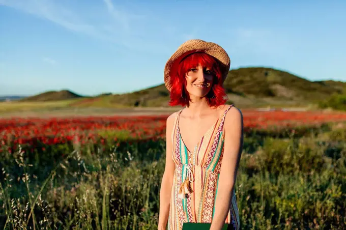 Smiling redheaded woman standing at poppy field