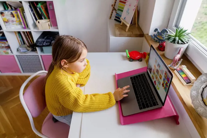 Girl using laptop on desk while learning at home