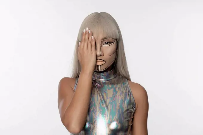 Cyborg woman covering eye with hand against white background