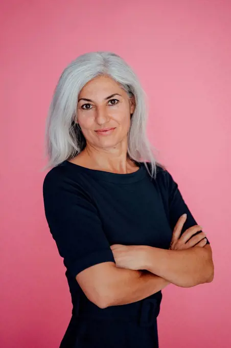 Female professional with arms crossed standing by pink background