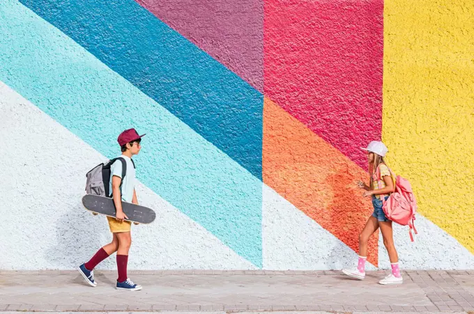 Girl and boy with backpacks walking on footpath