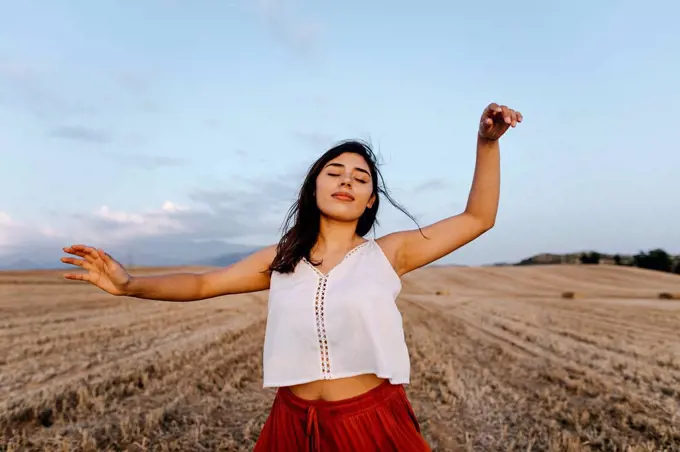 Woman with hand raised and eyes closed dancing at field