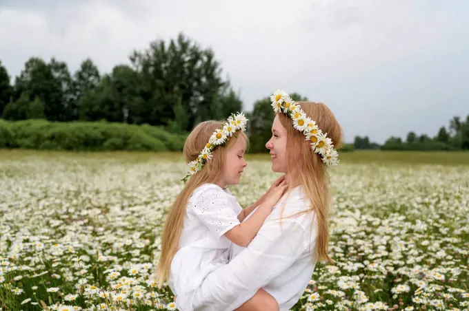 Smiling mother carrying daughter at chamomile field