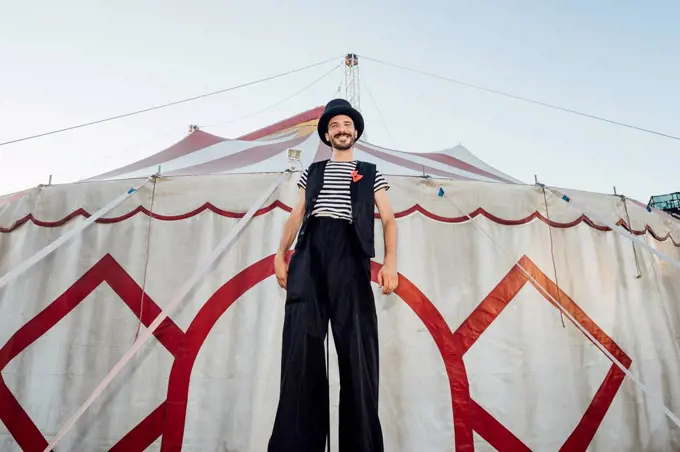 Male artist standing with stilts in front of circus tent