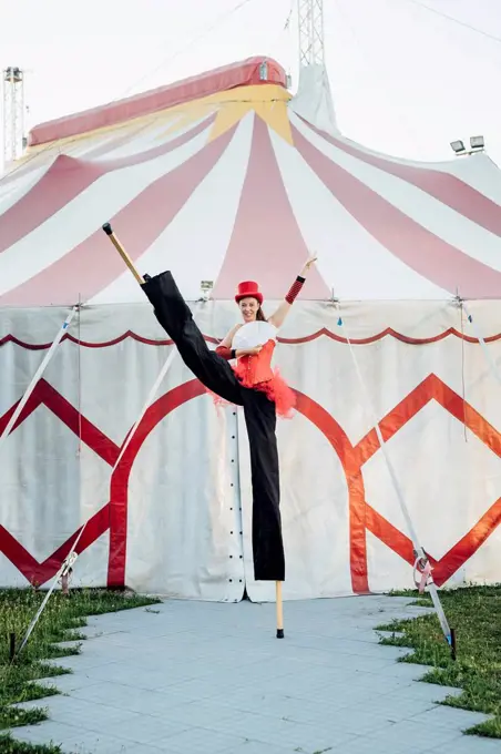 Female artist holding hand fan while standing with stilts in front of tent