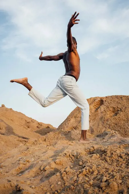 Shirtless man with arms outstretched dancing on sand