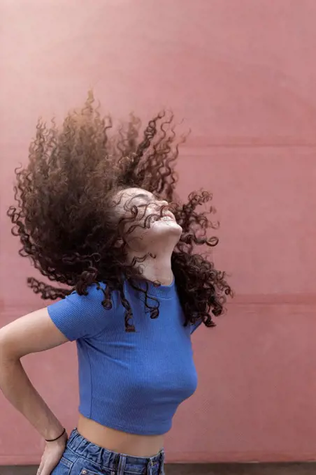 Young woman tossing hair in front of wall