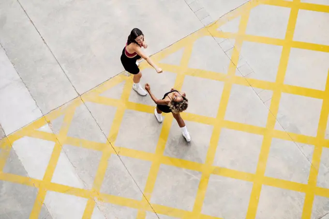 Multi-ethnic female friends boxing on yellow patterned footpath