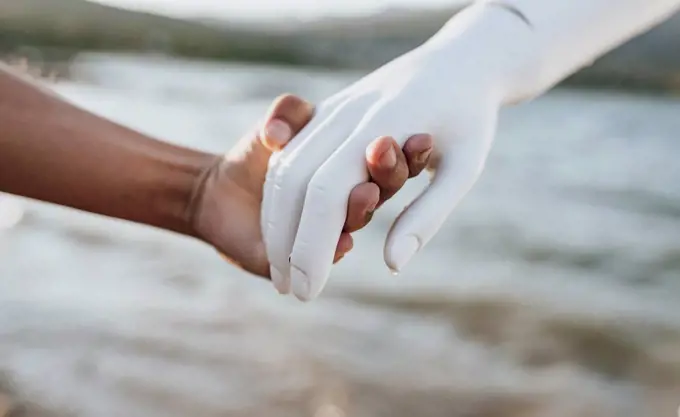 Young woman holding hand of robot