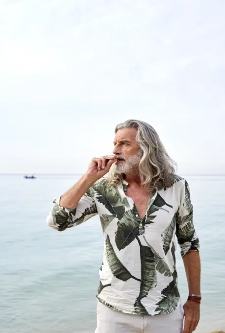 Mature man with gray hair smoking near sea at beach