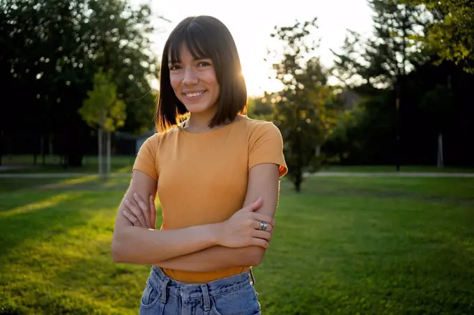 Smiling young woman standing with arms crossed at lawn