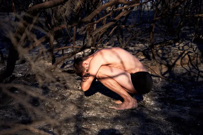 Shirtless man crouching on forest floor