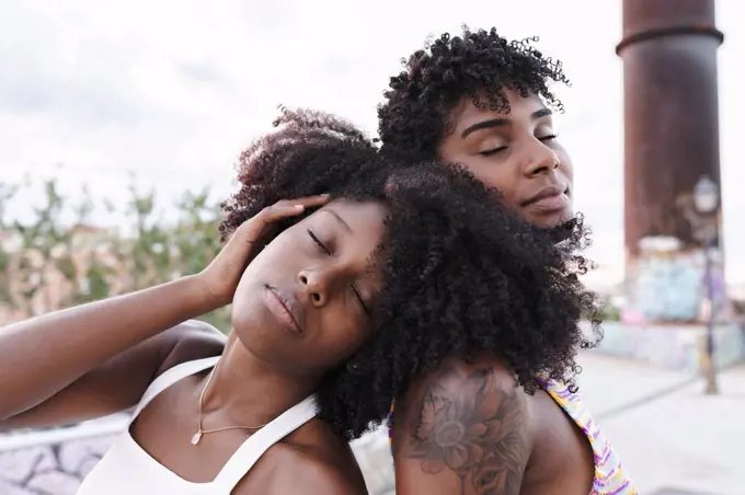 Afro woman with eyes closed leaning on shoulder of friend