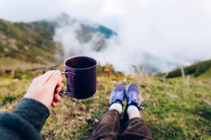 Woman holding cup of tea while sitting on mountain