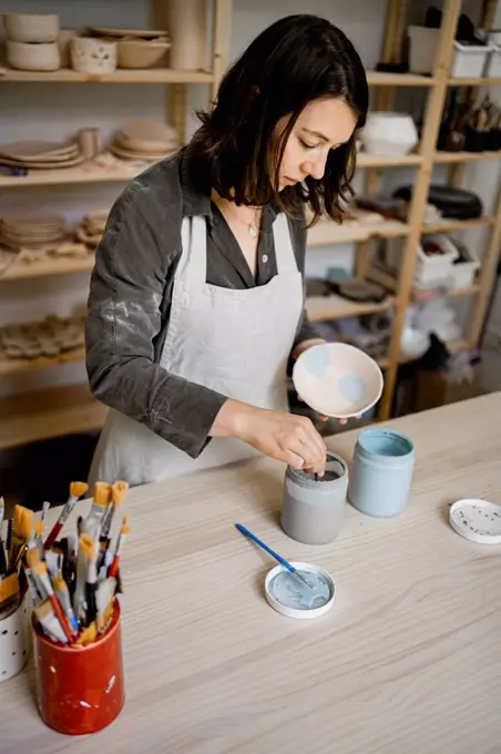 Female craftsperson painting bowl on workbench