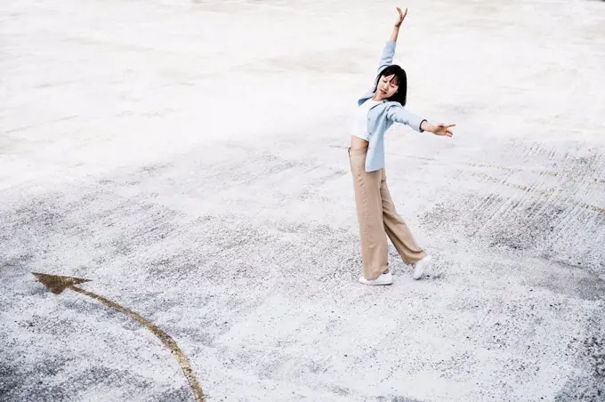 Teenage girl with arms outstretched dancing on parking garage rooftop