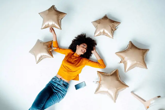 Smiling woman amidst star balloons lying on floor at home