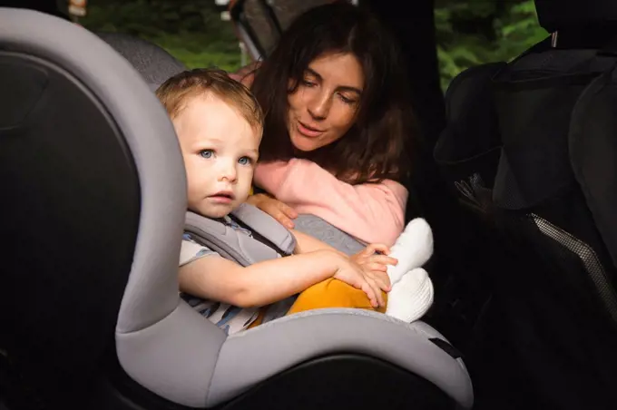 Mother talking to male toddler sitting on baby seat in car