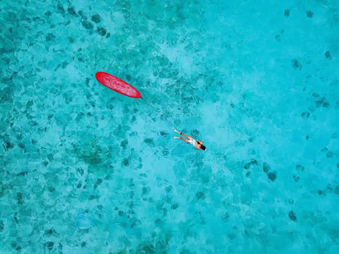 Woman with surfboard swimming in sea at Huraa island, Maldives