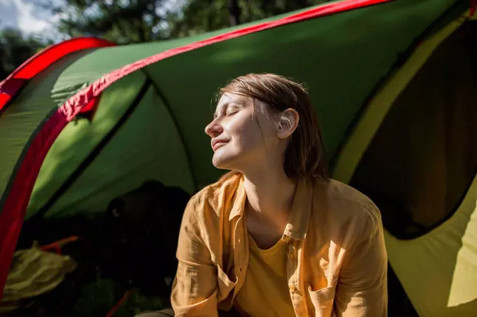 Smiling woman with eyes closed sitting at tent entrance