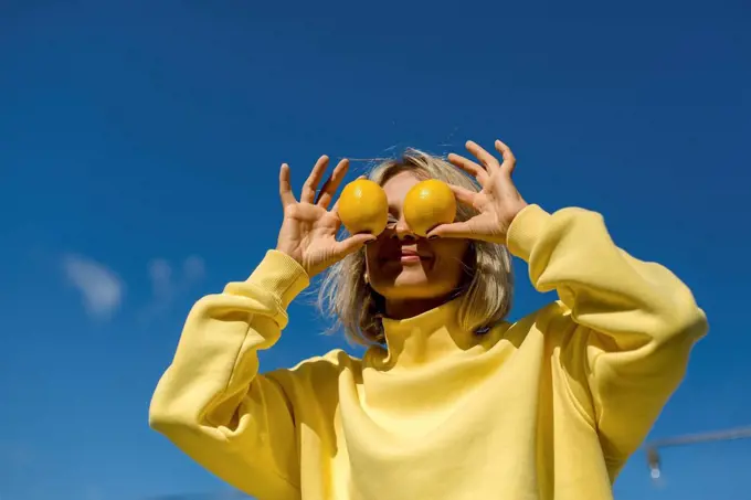 Mid adult woman covering eyes with lemon during sunny day