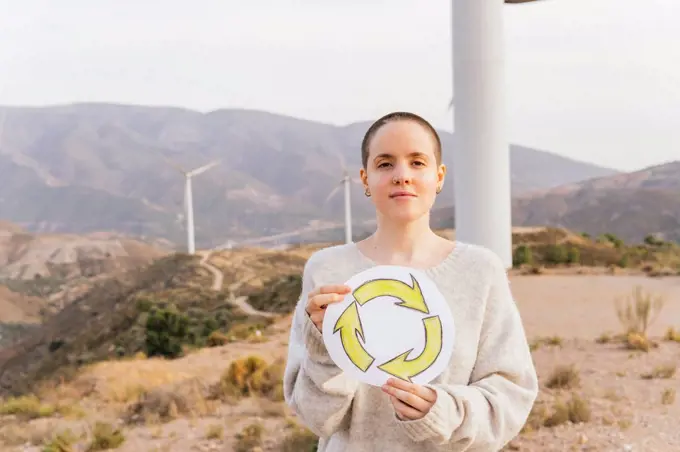 Shaved head woman holding recycling sign drawing at wind farm