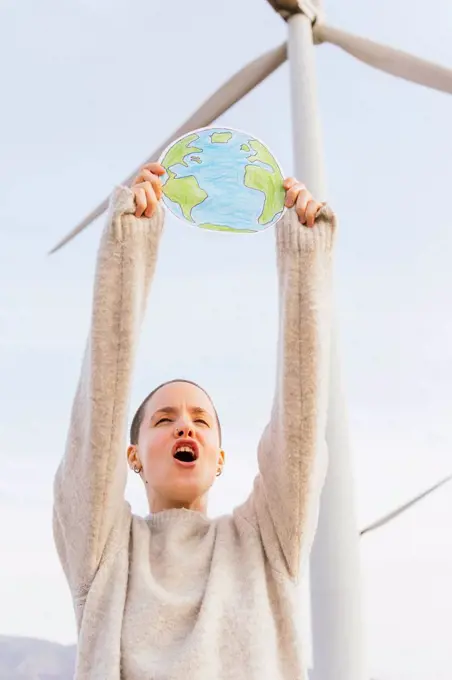 Woman screaming while holding earth drawing at wind turbine
