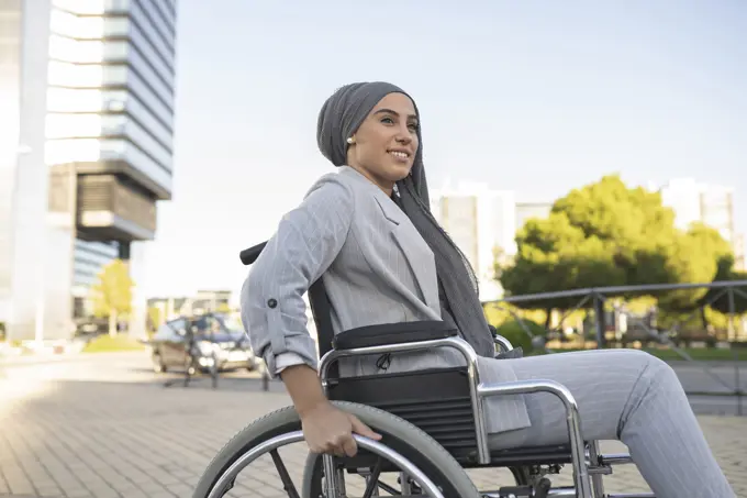 Smiling disabled woman sitting on wheelchair at footpath