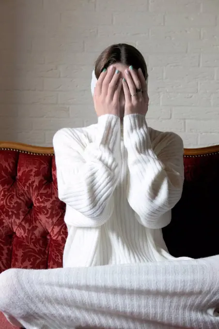 Teenage girl covering face with hands on sofa